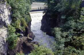 Auf der Brücke über die felsige Klamm stehen 3 Personen; unter ihnen das tosende Wasser des Lechfalls.